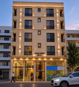 Stone-clad residential building with lit balconies, signed Anum Homes 86-C